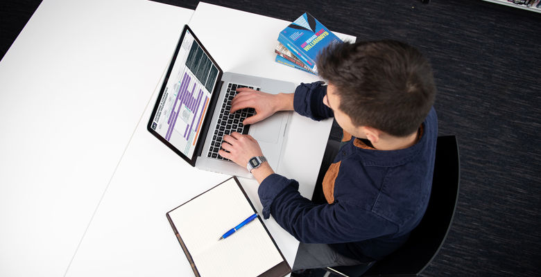 Student at a desk in the library with their laptop open, looking at Edinburgh College progression maps on the screen.