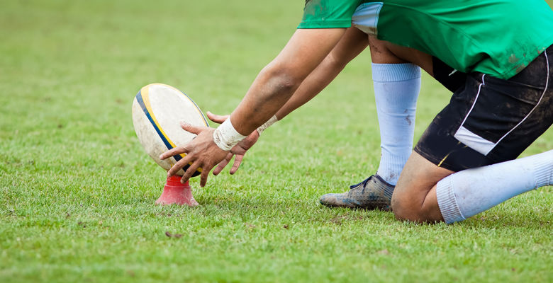 Sport student setting up a rugby ball for a shot on the pitch.