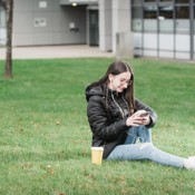 A young student is sitting on the grass looking at their phone at Granton campus. 